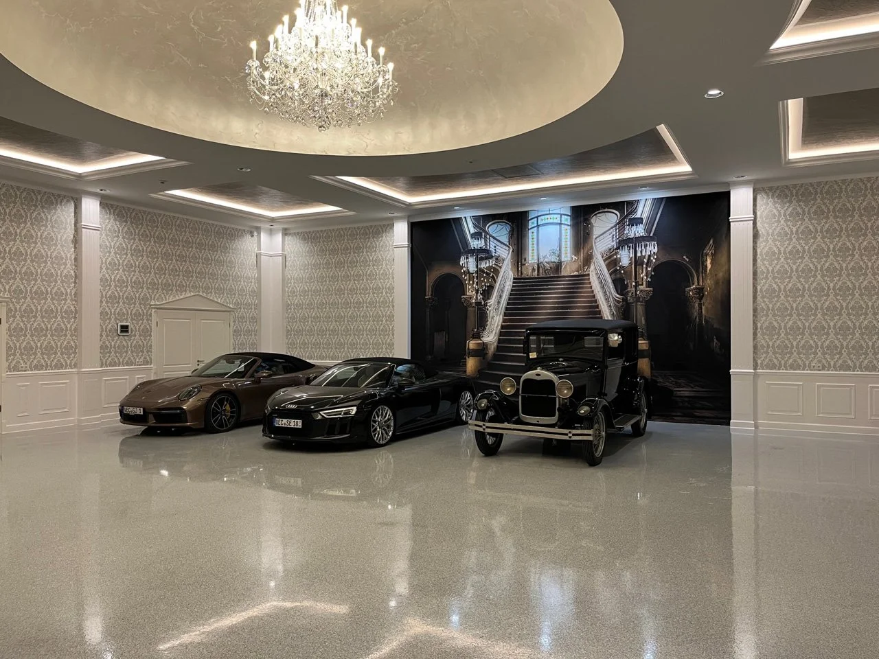 Innenraum mit drei Autos, eine große weiße Decke mit Kronleuchter, weiße Tapeten mit Muster und großem Wandbild einer viktorianischen Treppe.