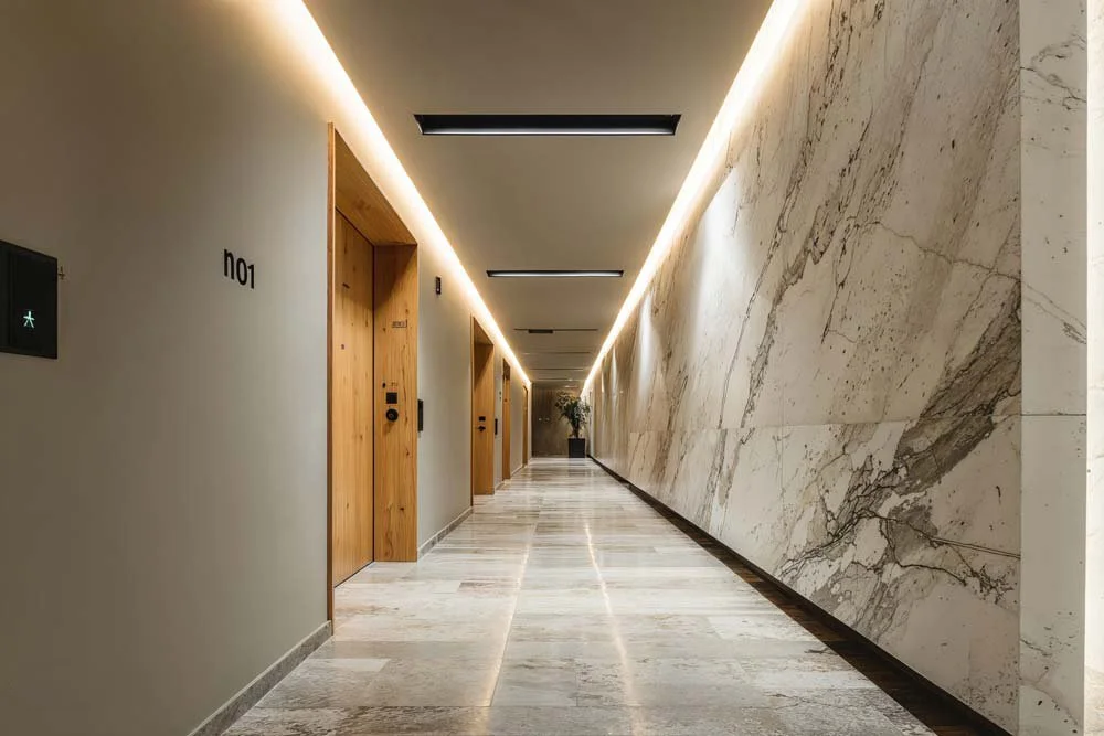 Heller, moderner Flur mit weißen Wänden, Holzaufzügen und Marmorbodengranit mit LED-Beleuchtung an der Decke.