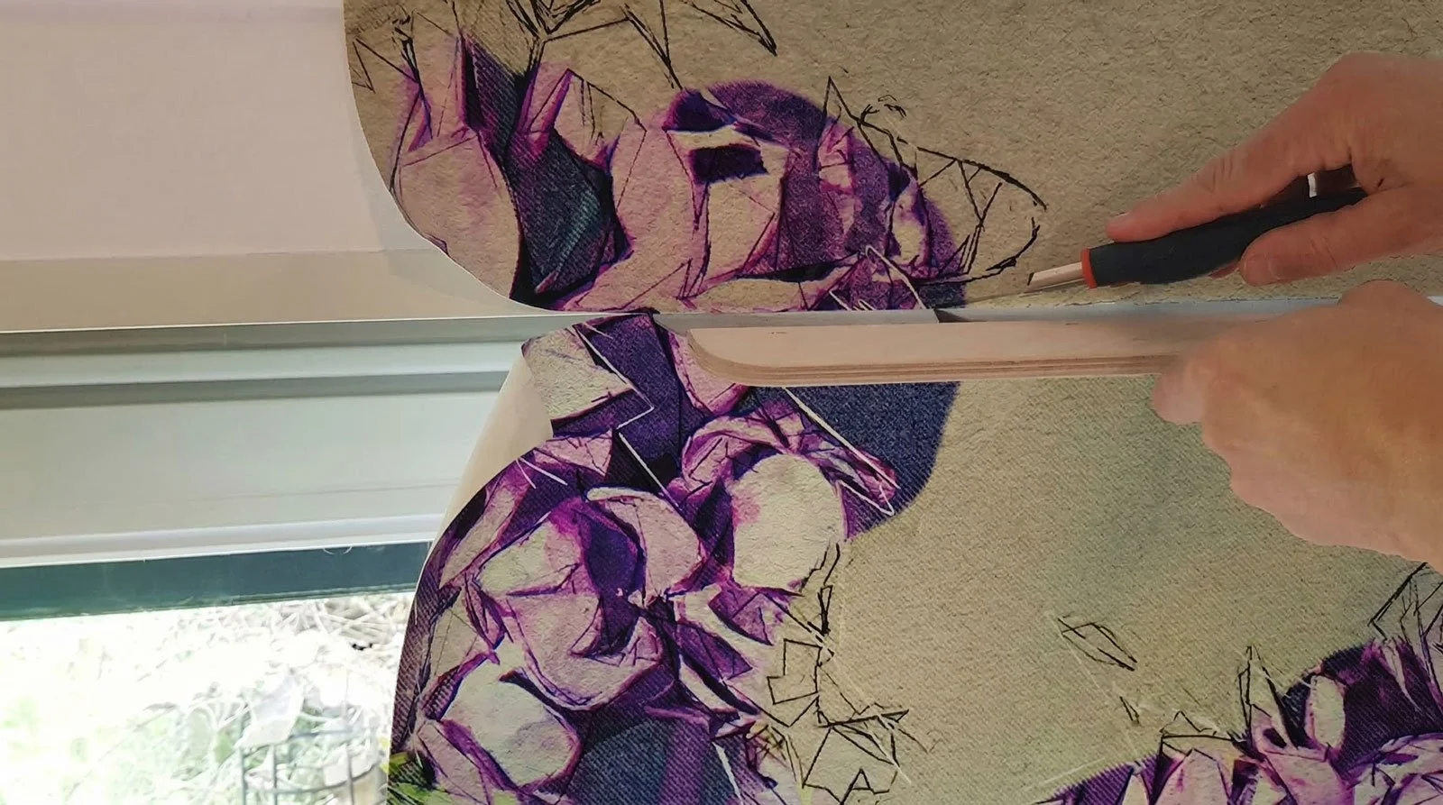 Person arbeitet an einem Stoff mit einem Blumenmuster, die Stoffbahn wird auseinander gezogen.