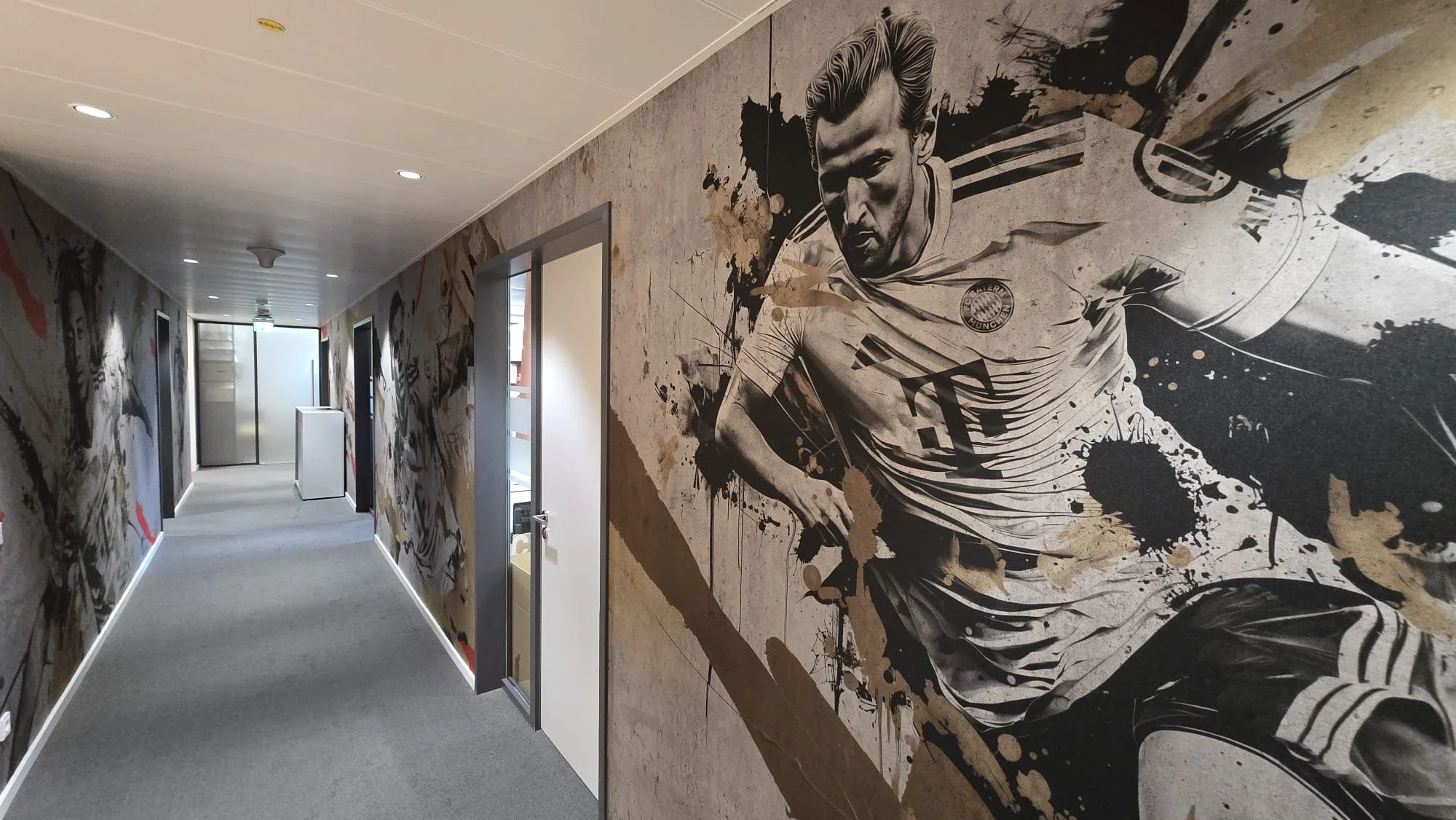 Flur mit Wandmalerei eines Fußballspielers in Aktion, schwarz-weißer Graffiti-Stil, im Hintergrund Türen und Fenster