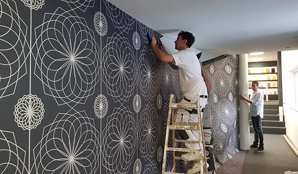 5. Poster ansetzen und verkleben.

Rolle mittig oder am Lot ausrichten.
Von oben nach unten in das Klebebett einlegen und gleichmäßig andrücken.
Die 5 cm Zugabe ermöglichen den Ausgleich kleiner Wandtoleranzen.
Solange der Kleber feucht ist, sind Kor