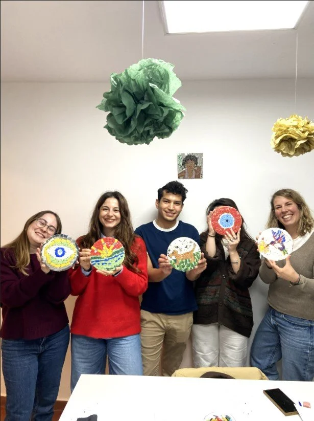 Grupo de seis personas en interiores sosteniendo cerámicas decoradas. Hay decoraciones en el techo y un cuadro en la pared.
