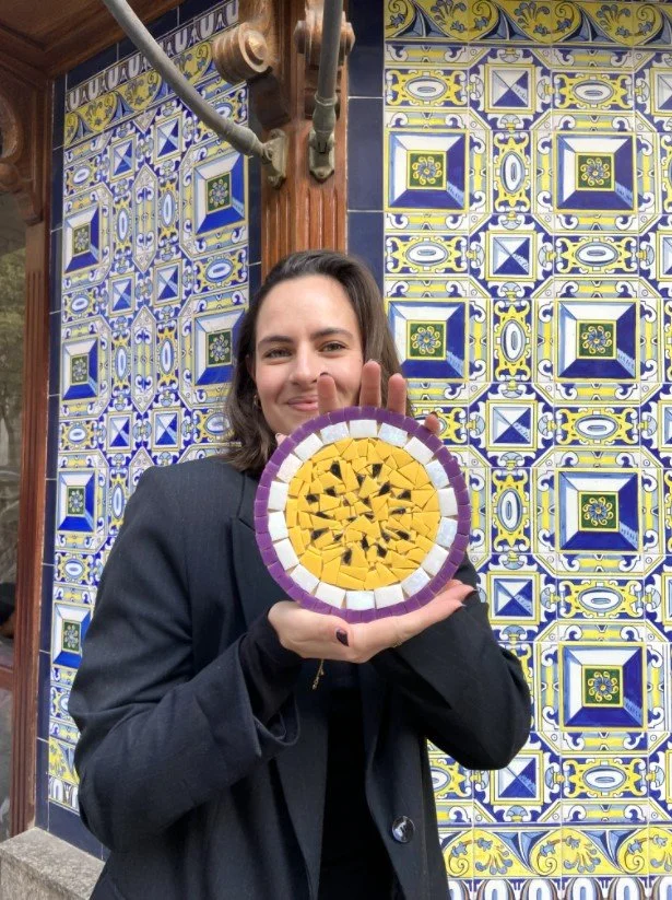 Mujer  con mosaicos amarillos, blancos y morados, en un fondo de azulejos coloridos con patrones geométricos.