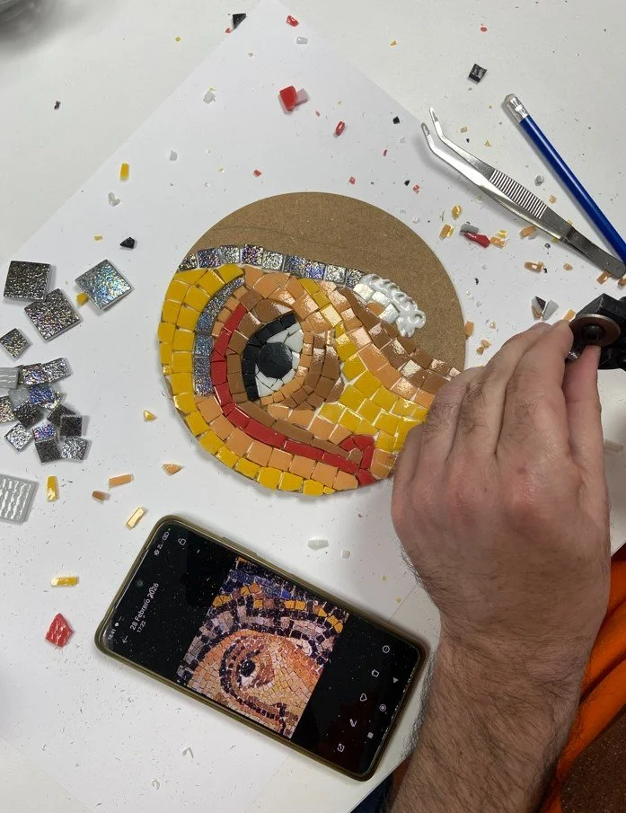 Persona creando un mosaico de una cara de pájaro con pequeños azulejos de colores en una mesa de trabajo.
