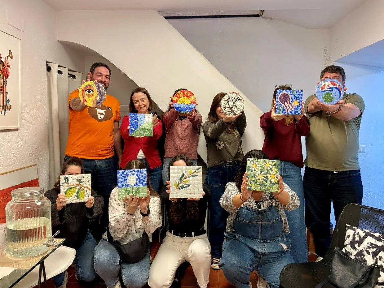 Grupo de personas mostrando artesanías de cerámica y mosaico decoradas con diferentes diseños y teselas en un espacio chulo. Clases de mosaico en Madrid