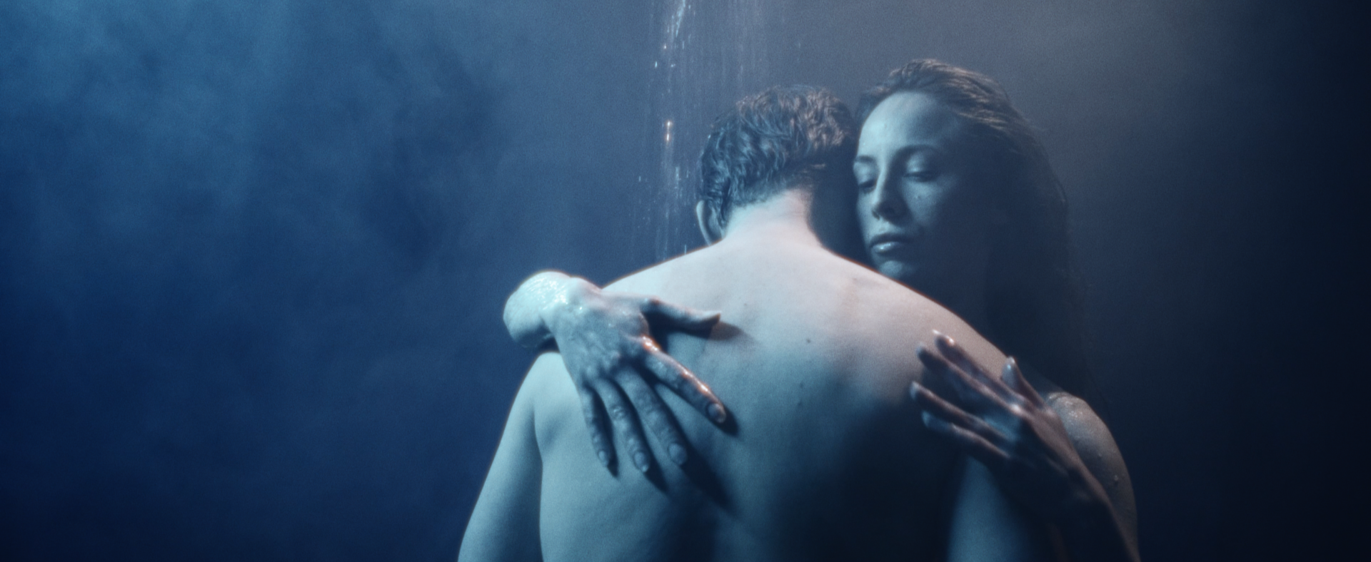 A man and woman embracing underwater, with the woman holding onto the man's back and the man's face hidden.