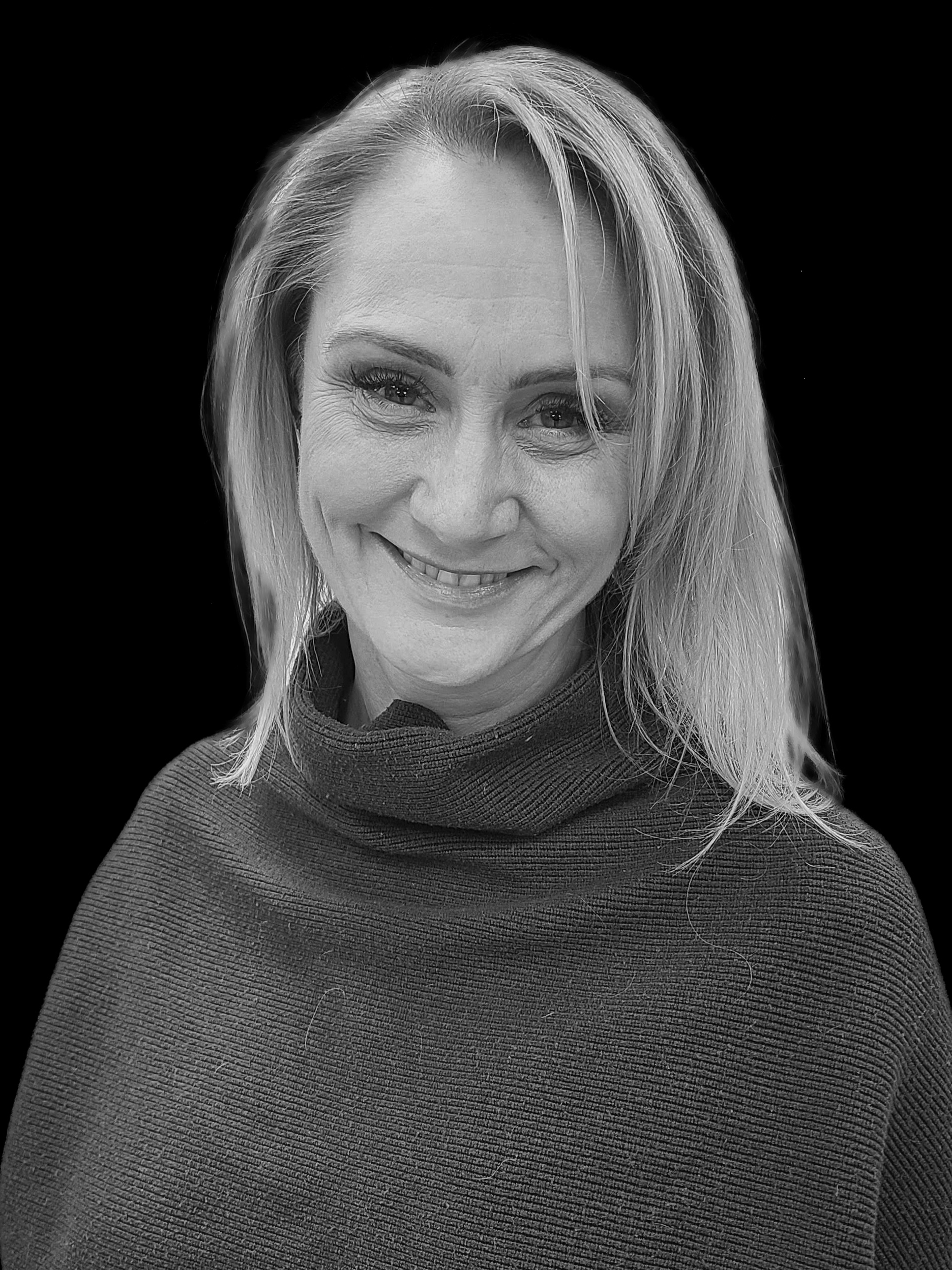 Black and white portrait of a smiling woman with shoulder-length hair, wearing a turtleneck sweater, against a dark background.