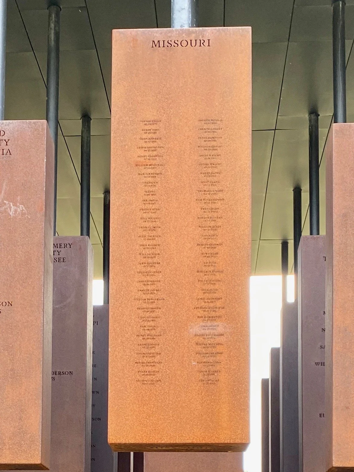 Copper column hanging from an overhead platform with the names of Missouri lynching victims engraved on it.