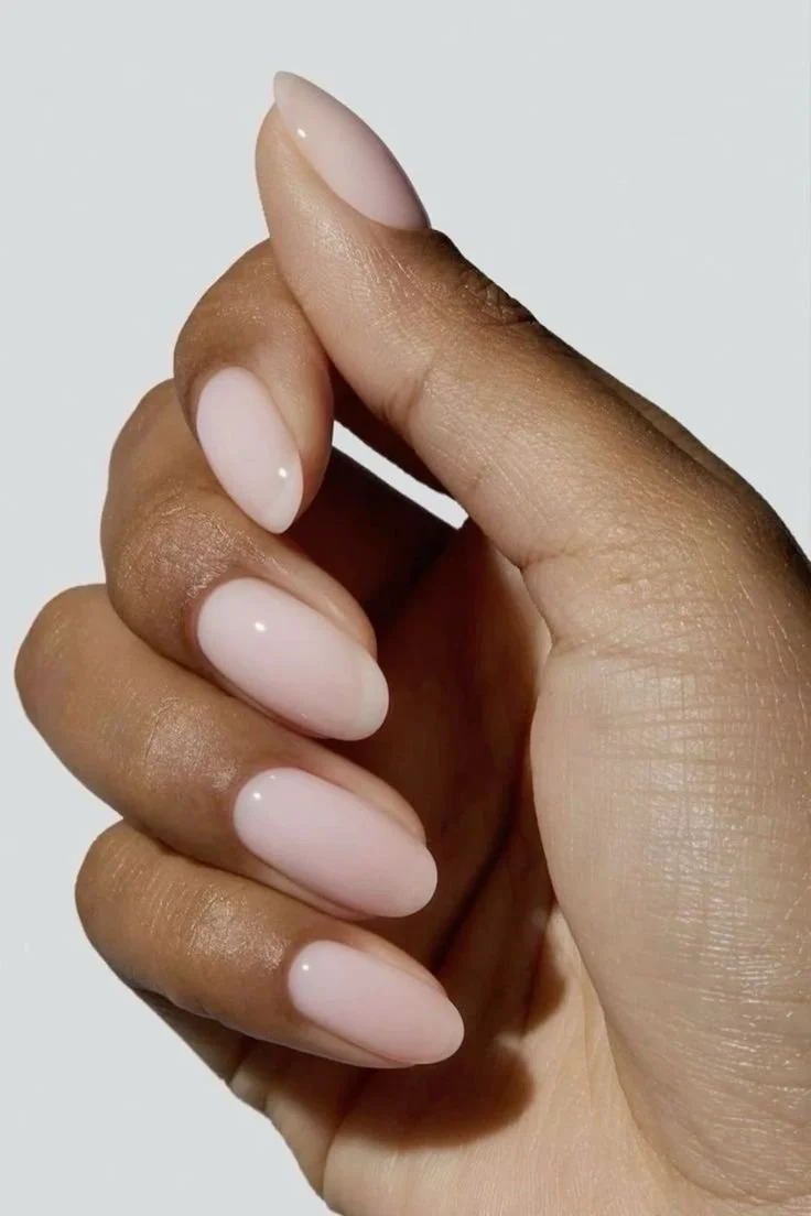 Unghie curate con smalto rosa chiaro su una mano con pelle scura, messa in evidenza in primo piano.