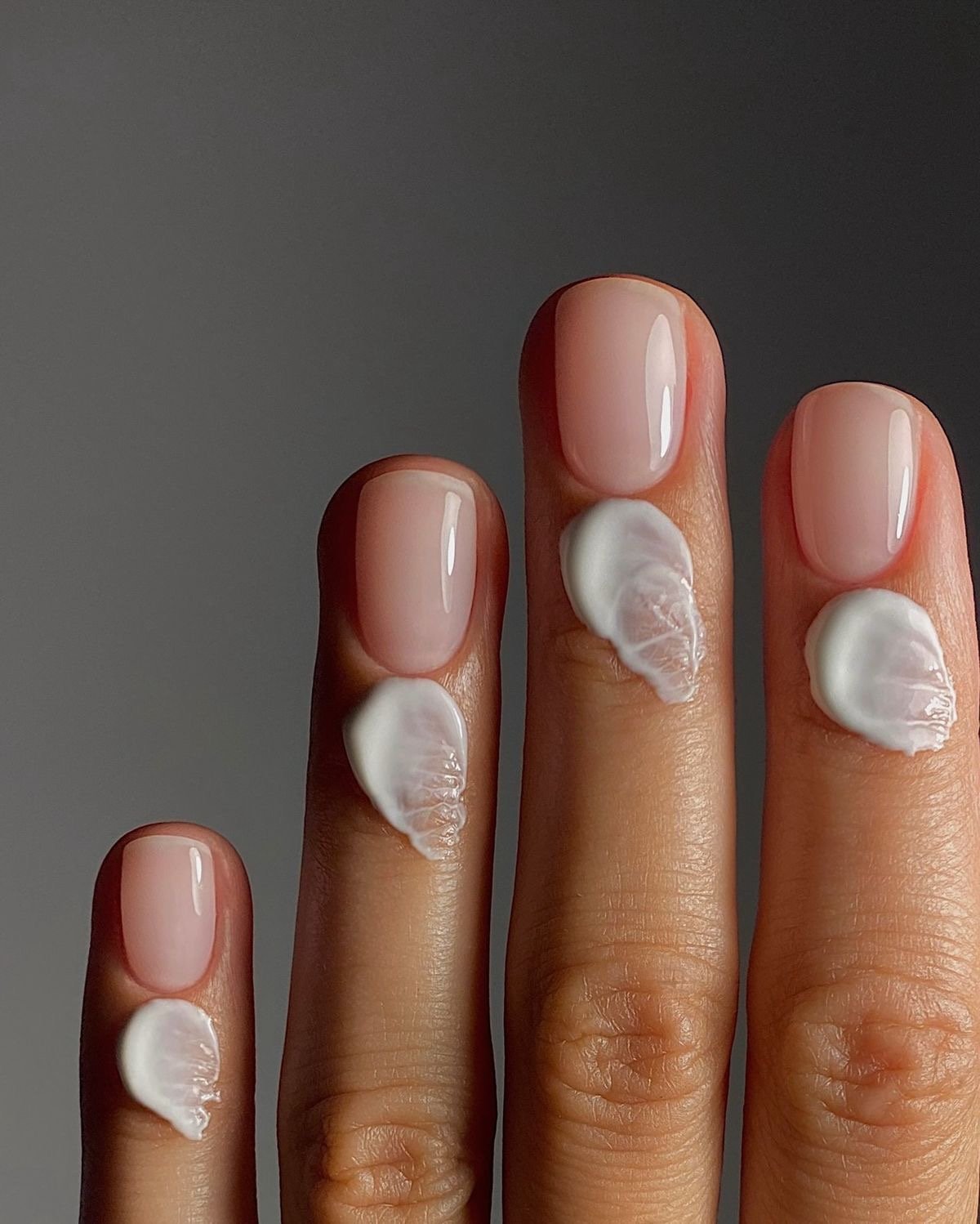 Dita con smalto naturale e crema bianca applicata sulle unghie.