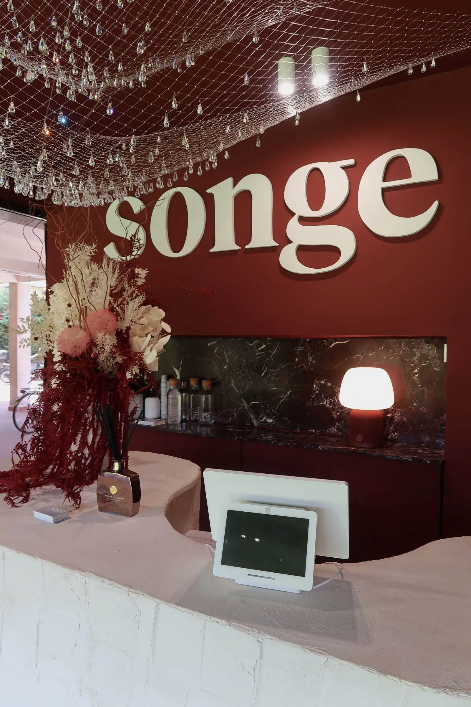 Decorazioni di Natale con una composizione di fiori e un'illuminazione calda, sullo sfondo la scritta 'Song' in bianco su parete rossa, con un lampadario di cristalli e un tavolo con dispositivo elettronico.