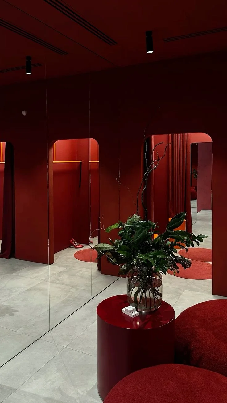 Interno con pareti rosse, specchio e un vaso con piante verdi su un tavolino rosso.