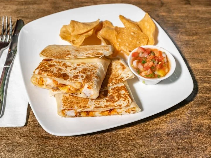 Plate with tortilla wraps, potato chips, and salsa on a wooden table.