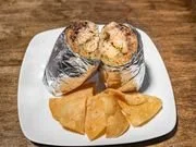 A plate with baked potato wrapped in foil, tortilla chips, and a small container of sour cream.
