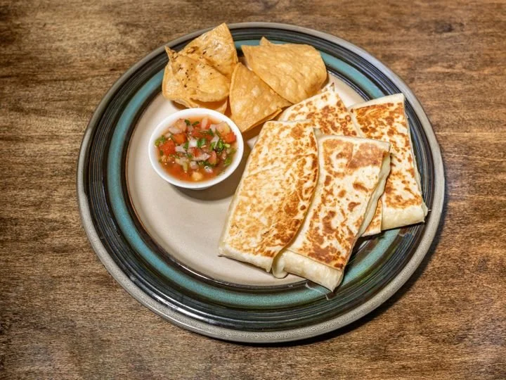 Plate with five quesadillas, tortilla chips, and salsa in a small bowl on a wooden table.
