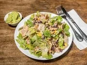 Bowl of salad with lettuce, grilled chicken, cheese, and croutons on a wooden table.