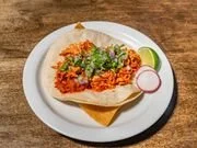 Taco with ground beef, shredded cheese, lettuce, chopped tomatoes, and sliced radish on a white plate with lime and cilantro garnishes
