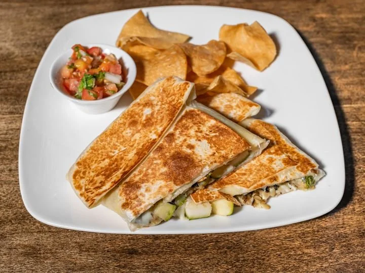 A plate of quesadilla with a side of chips and salsa on a wooden table.