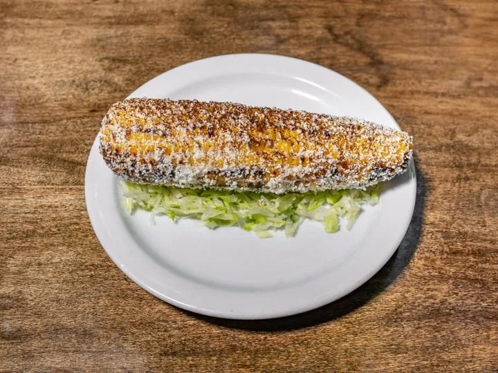 Fried cheese stick on a white plate above shredded lettuce, placed on a wooden surface.