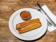 Churros with a small cup of dipping sauce on a white plate, with fork and knife on a paper napkin.