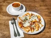 Plate of nachos topped with cheese and sour cream, served with a small bowl of chili, on a wooden table.