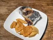 A white plate holding two pieces of salam and a serving of potato chips, on a wooden table.