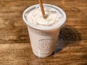 A cold beverage in a clear plastic cup with a lid and straw, resting on a wooden surface.