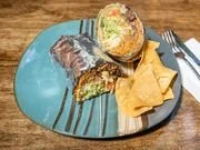 A plate with sliced cake, two triangular tortilla chips, and a gold-colored wrapped candy on a blue plate with a fork and knife.