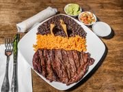 Plate of grilled steak, fried chicken, rice, guacamole, salsa, and sour cream on a wooden table.