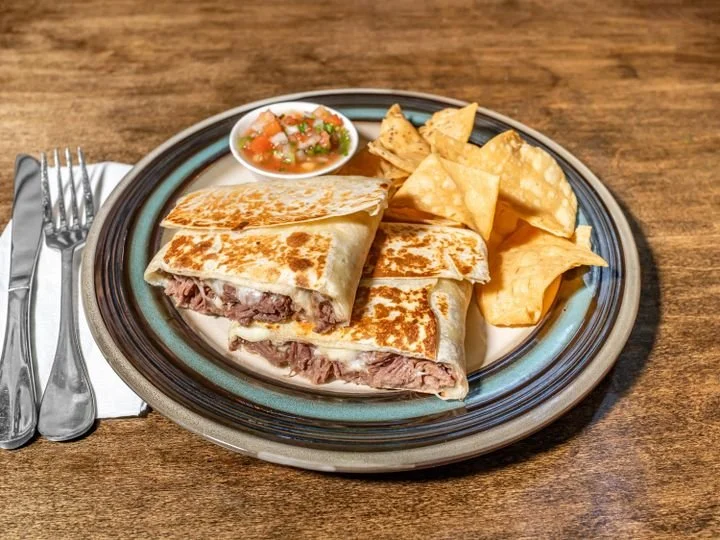 A plate with a quesadilla cut in half, served with tortilla chips and salsa, on a wooden table.