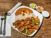 Plate of fried chicken with rice and vegetables, served with two small bowls of sauce on a wooden table.
