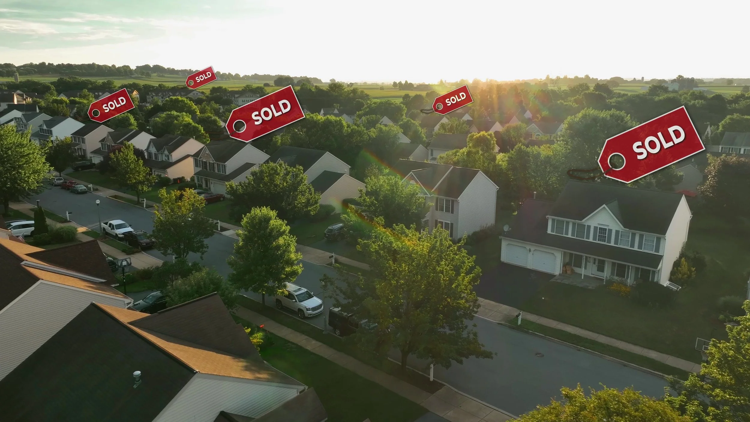 A neighborhood with houses and trees during sunset, with red tags labeled 'SOLD' floating above some homes.