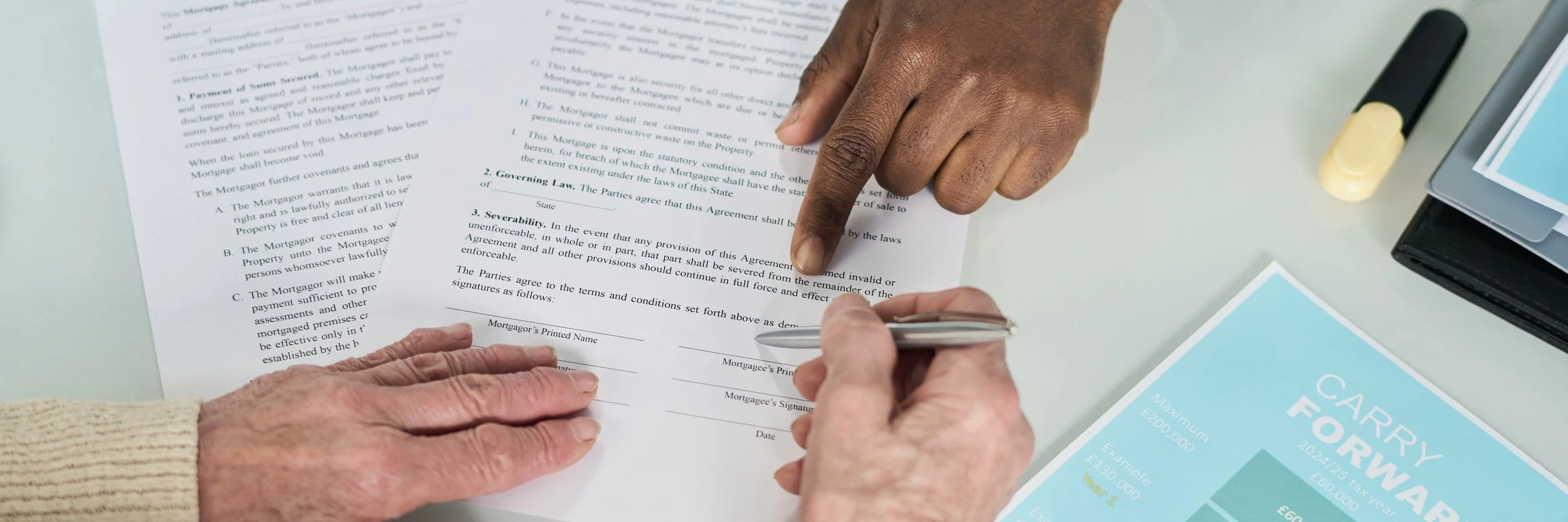 Close-up of hands signing a legal document at a desk, with workbook, pen, and documents around.