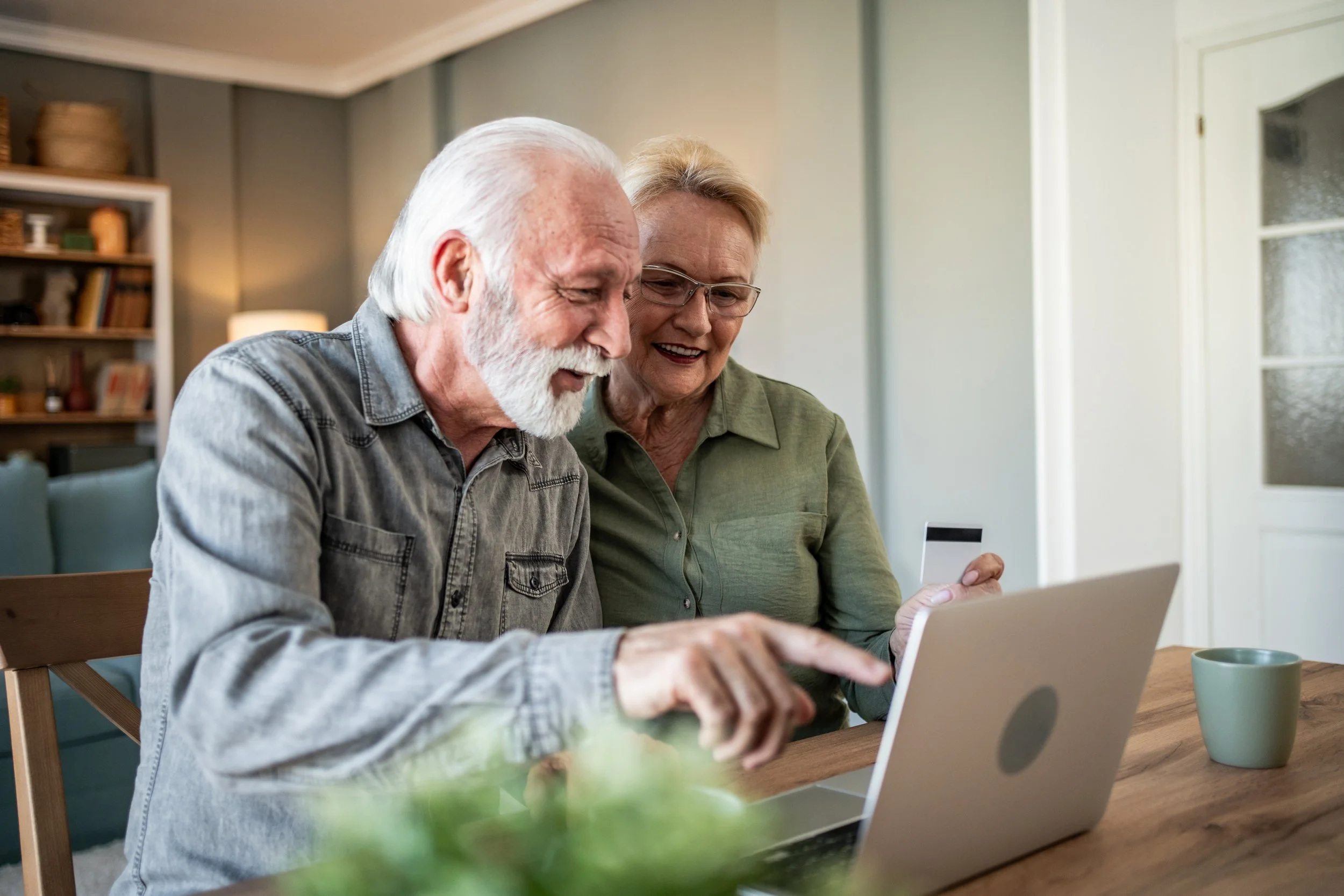 An elderly man and woman looking at a laptop together, smiling and enjoying their time.
