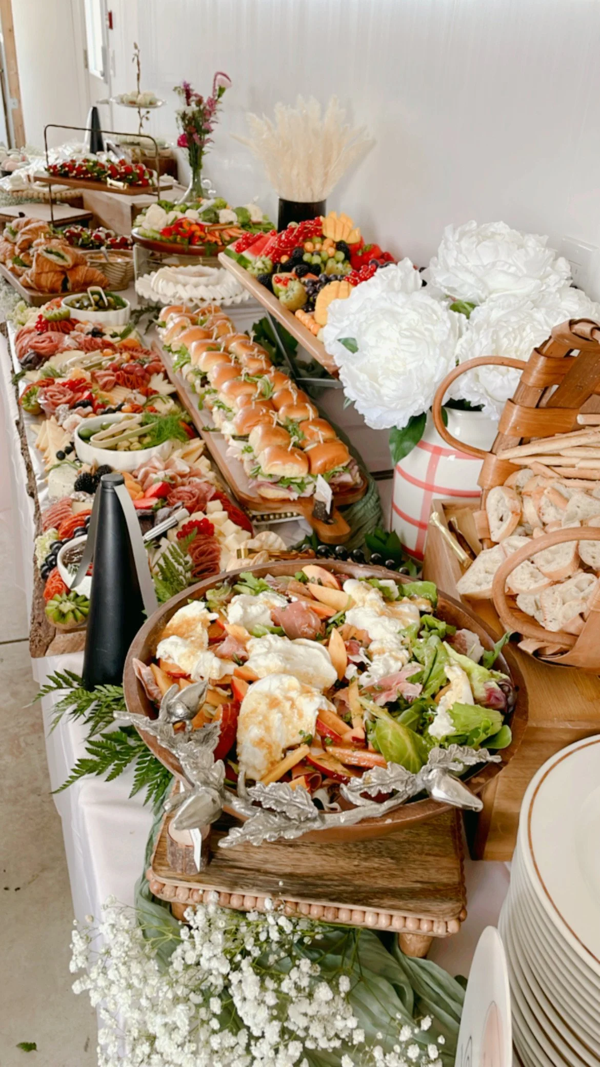 A table filled with various appetizers, salads, finger foods, and fruit platter at a buffet-style arrangement with flowers and decorative elements.