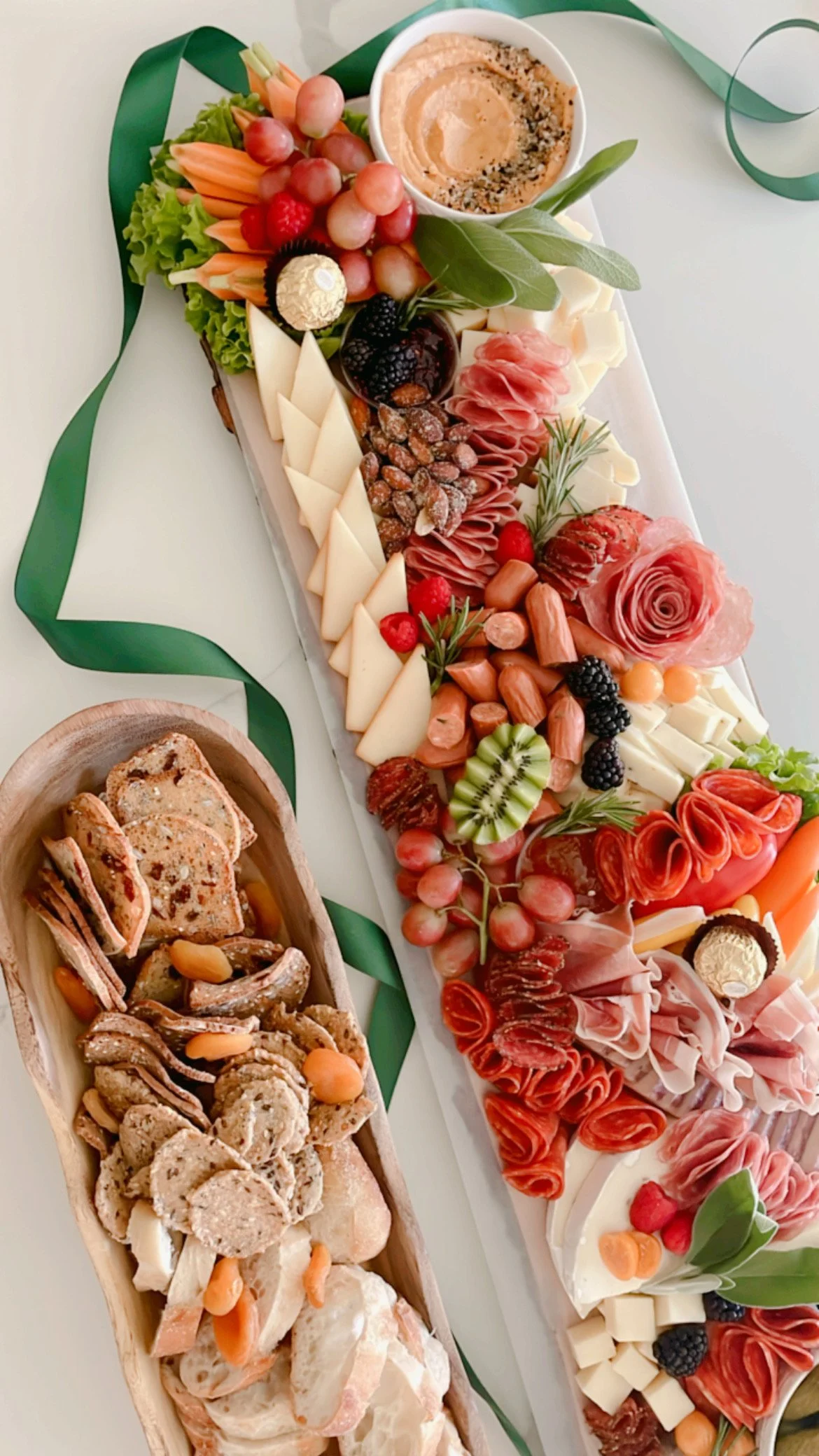A charcuterie board with assorted cheeses, meats, fruits, nuts, and garnishes. Smaller snack platters with sliced bread and savory snacks are included.