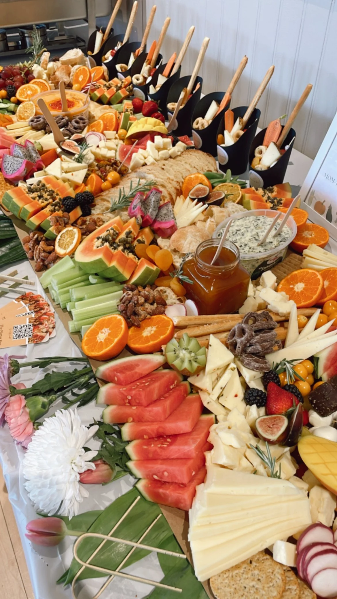 A table with a variety of fresh fruit, cheeses, crackers, honey, and dips arranged for a snack or buffet.