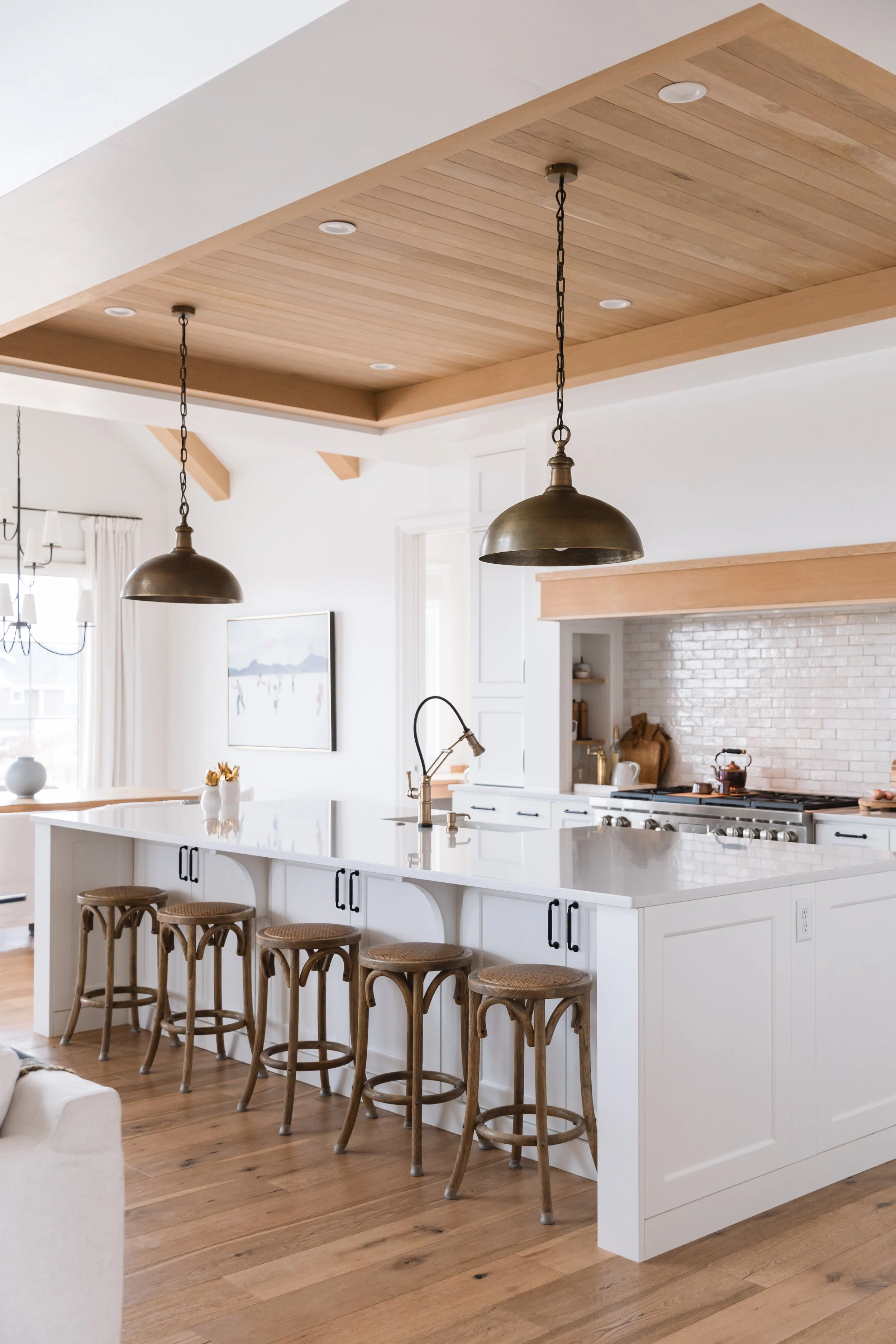Modern kitchen with white cabinets, a large island with a white countertop, wooden bar stools, and brass pendant lights.