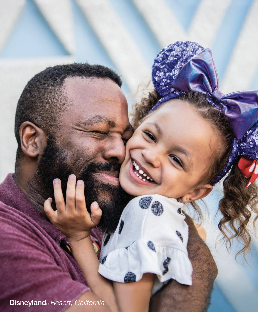 A man and young girl sharing a joyful hug at Disneyland Resort in California, with both smiling and showing happiness.