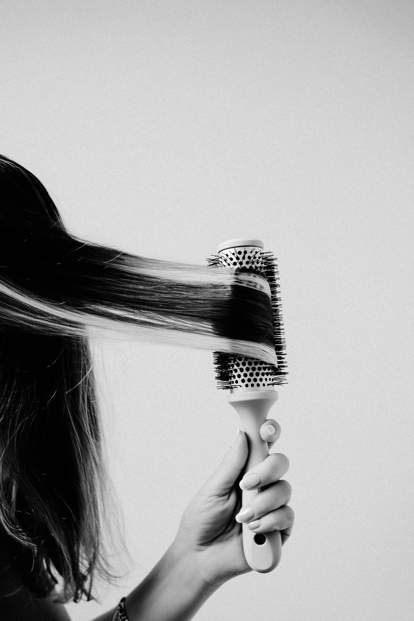 Black and white photo of a person with long hair using a round hairbrush to style their hair.