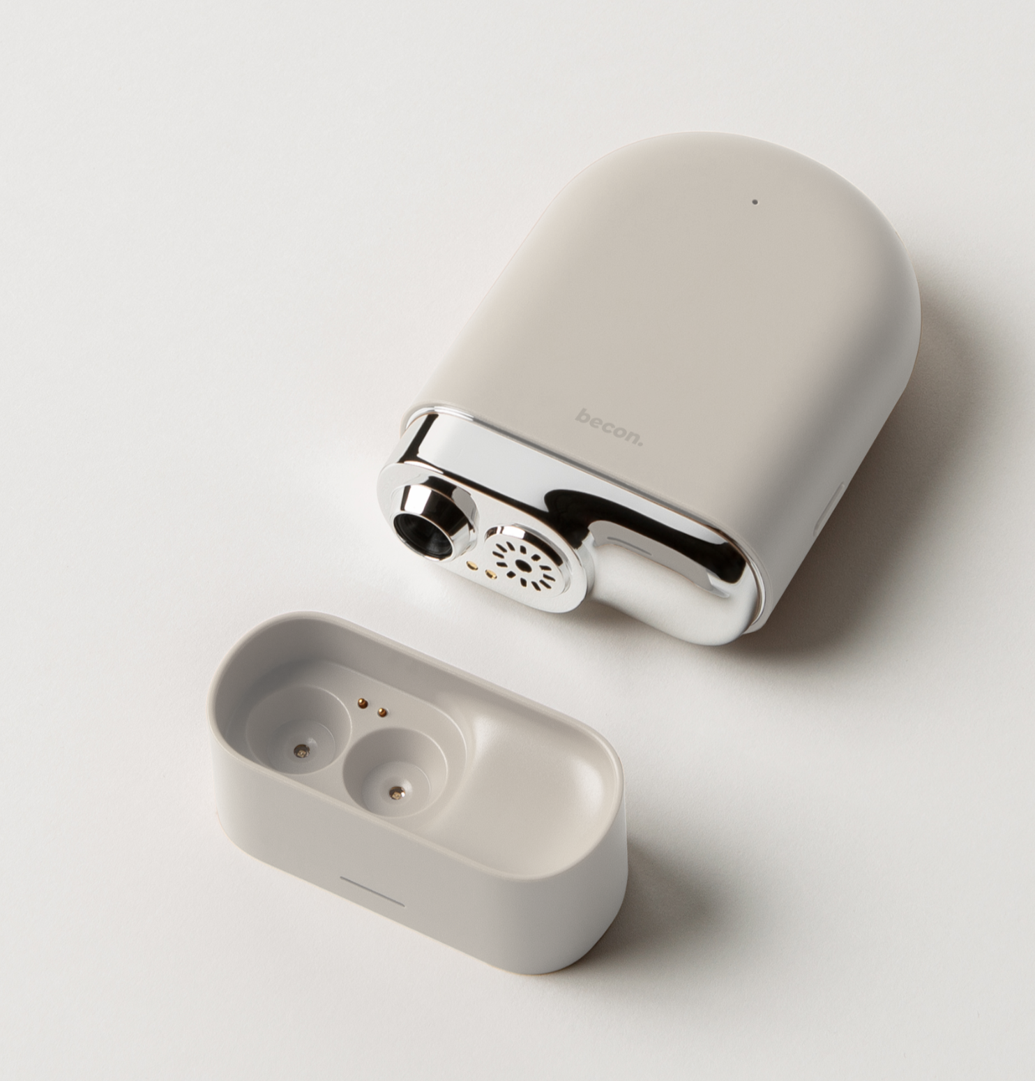 A white electronic device with a sleek design, accompanied by a separate white charging case with gold contact points, on a white surface.