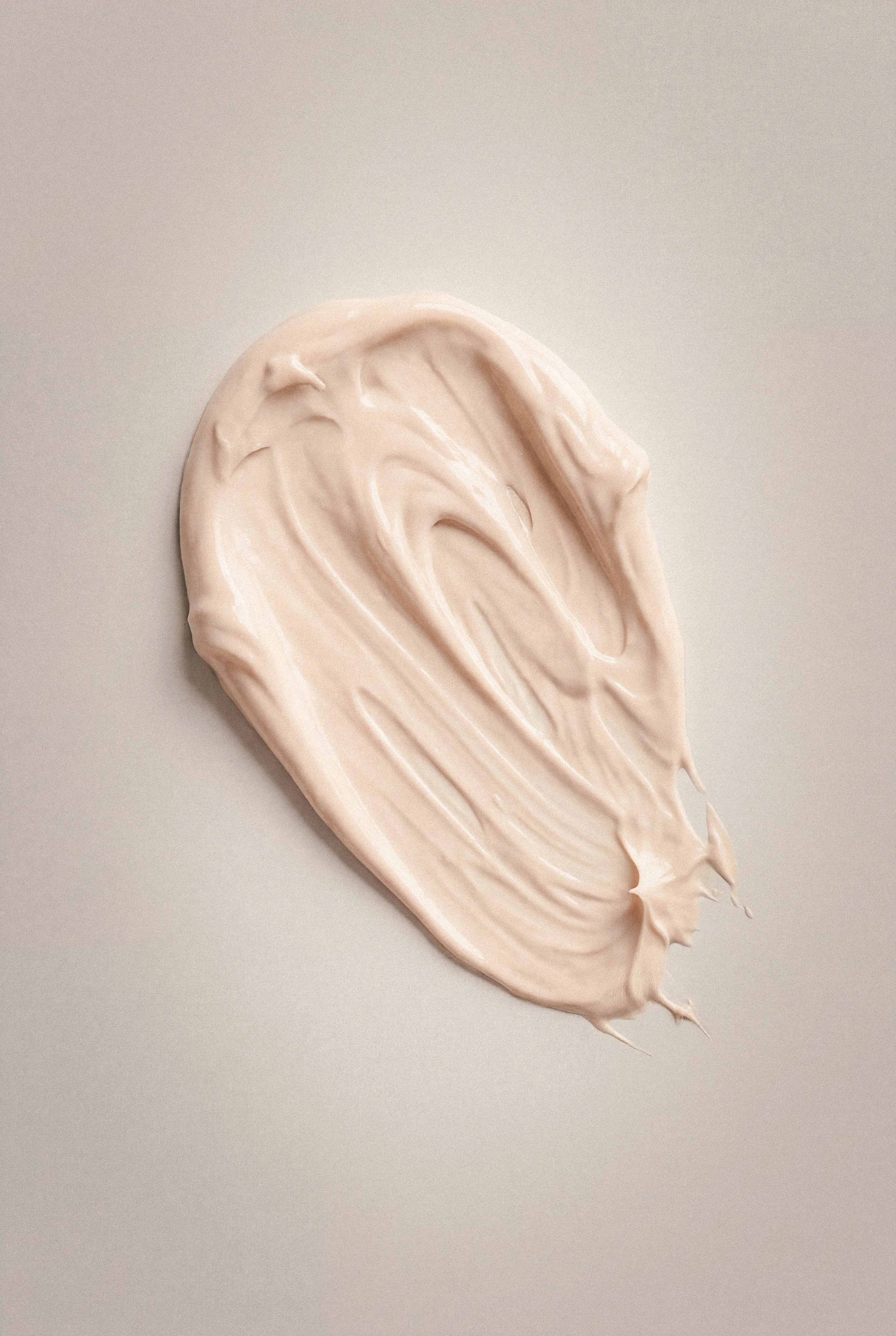 A large smear of beige-colored cream or lotion spread on a plain light grey surface.