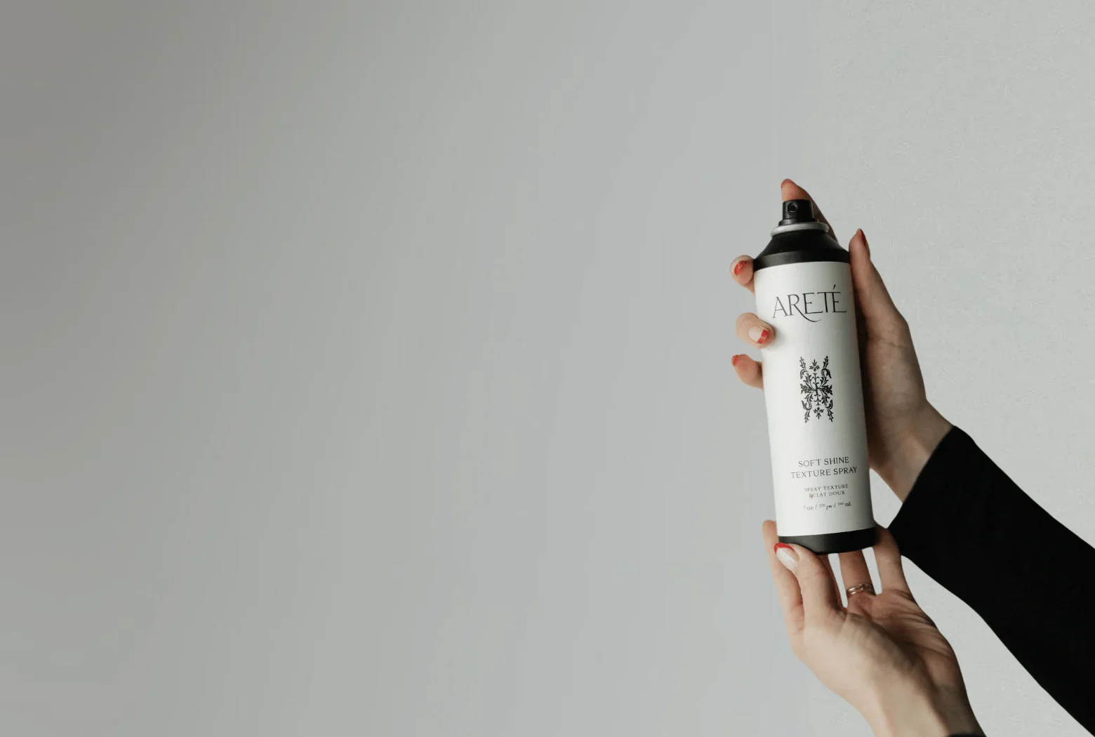 A hand holding a white can of ARETE Soft Shine Texture Spray against a plain, light-colored wall background.