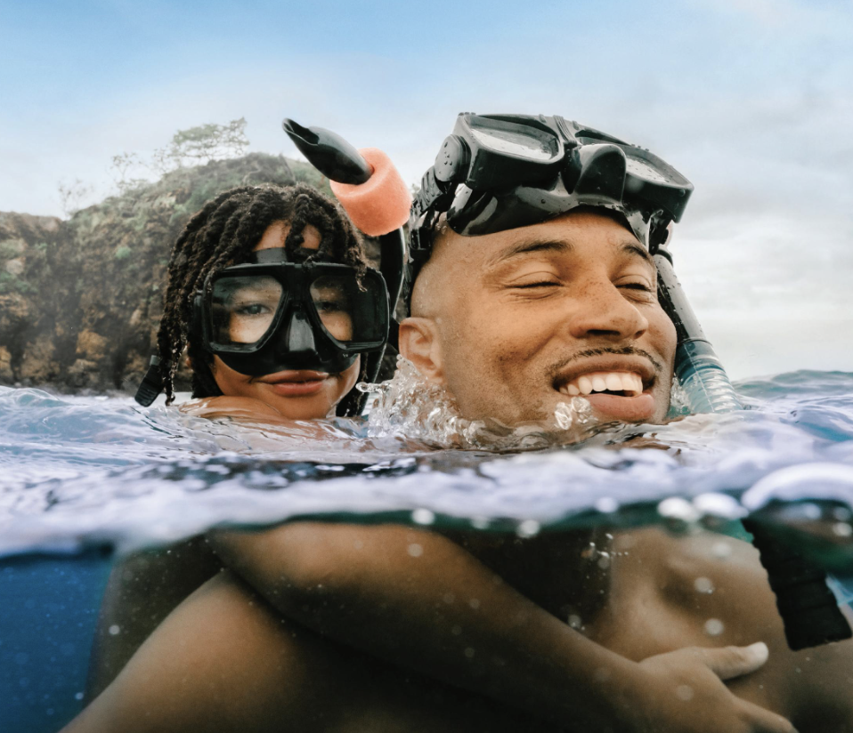 Two people snorkeling in the water near a rocky coastline, wearing snorkeling masks and fins, enjoying their time outdoors.