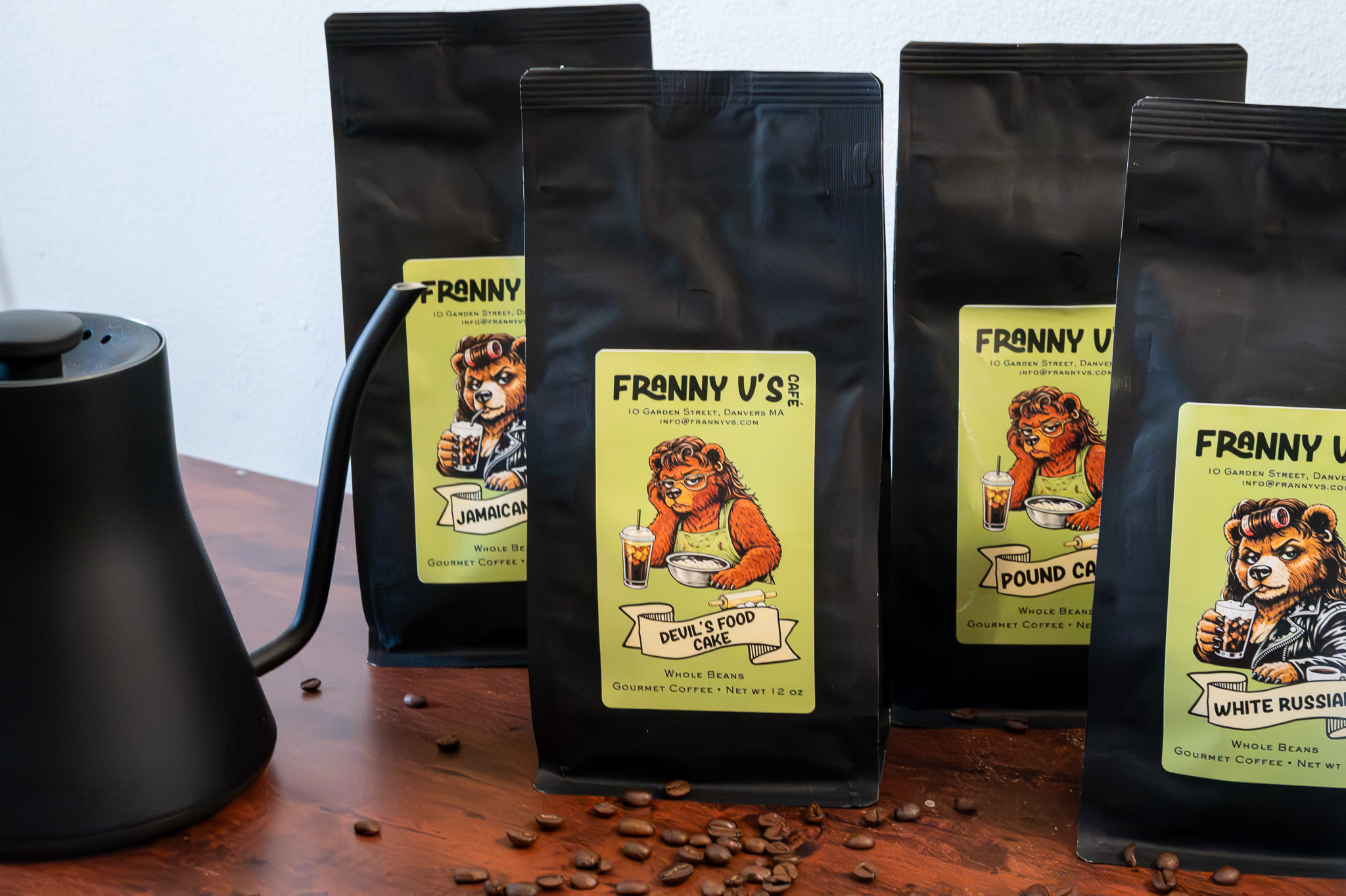 Multiple black coffee bags with colorful labels featuring cartoon bears, placed on a wooden surface with scattered coffee beans.
