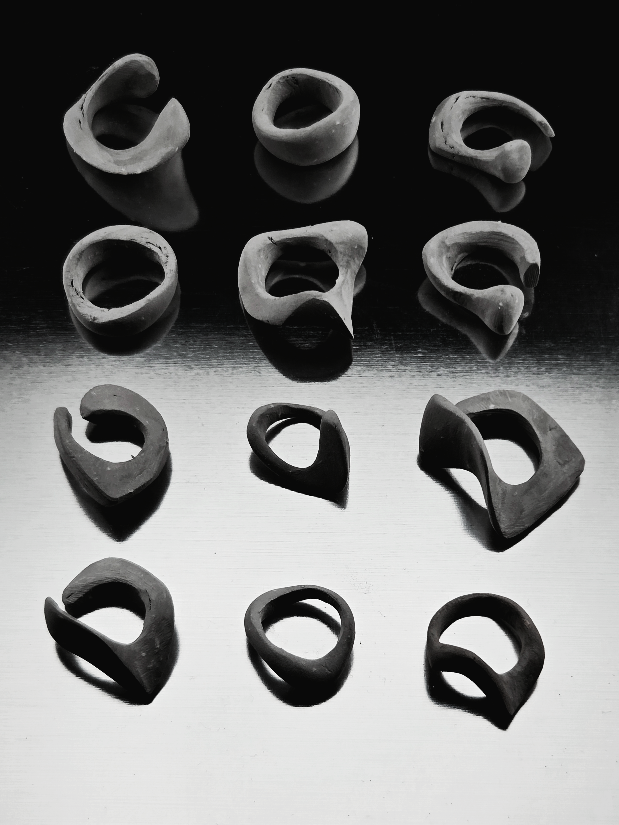 Six ear-shaped objects, some hollow and some solid, arranged on a reflective surface. The objects are in black and white, with varying sizes and shapes.