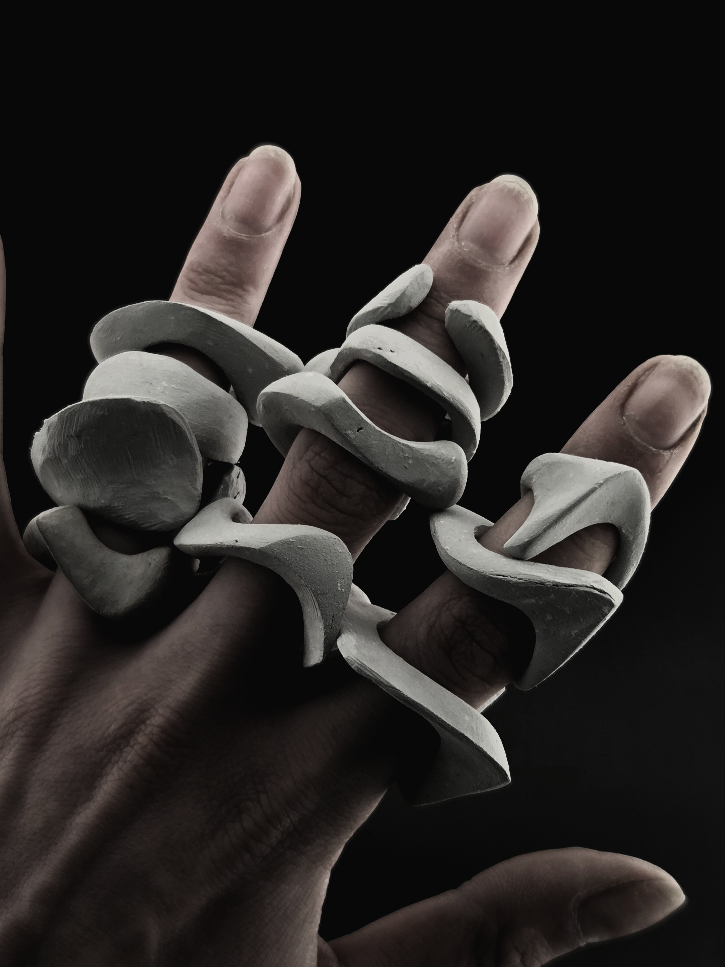 A close-up of a hand with fingers extended, adorned with layered white rings, against a black background.