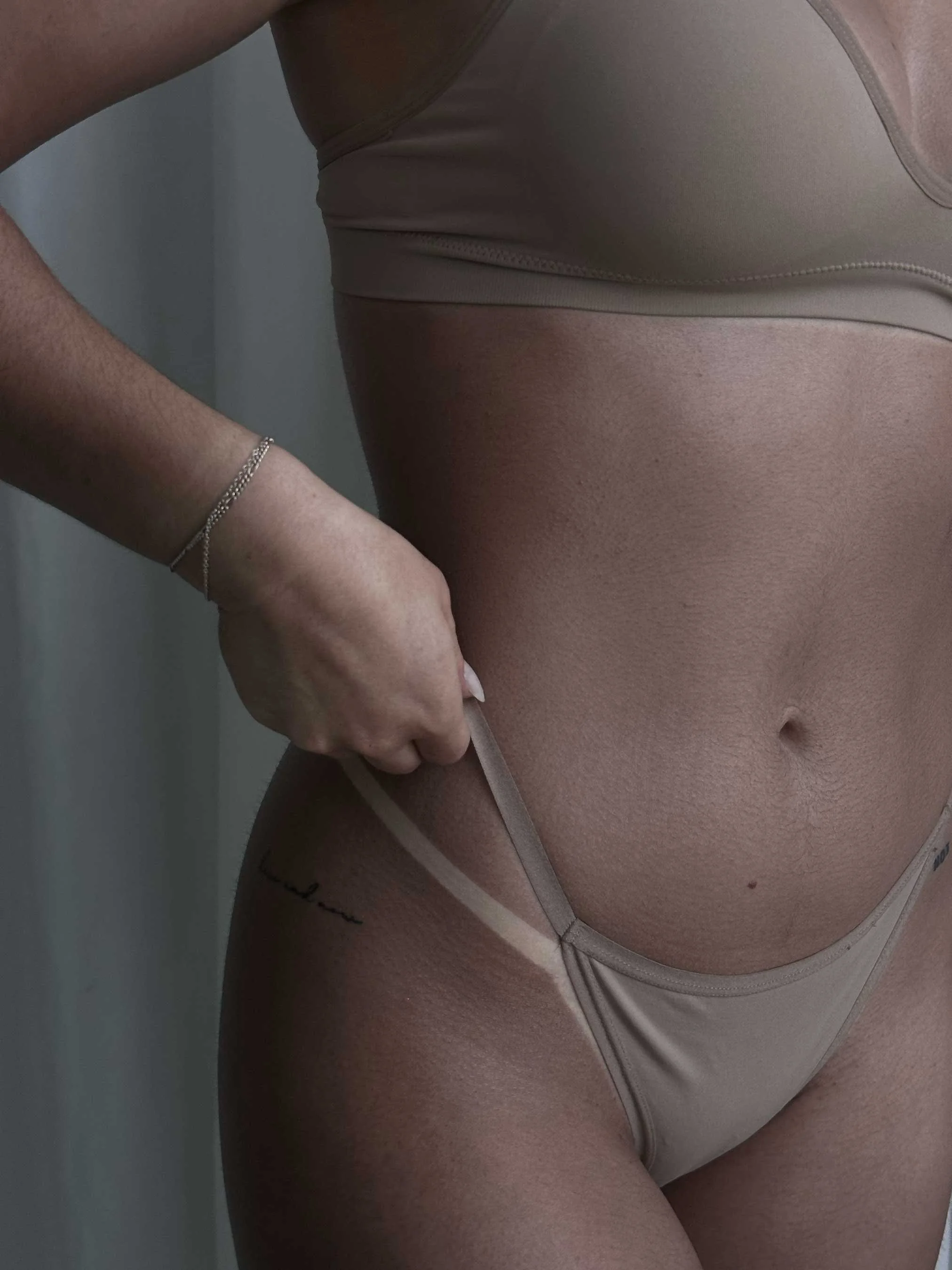 Close-up of a woman's lower torso and upper thigh, wearing beige underwear, showcasing her sunless tanner results.