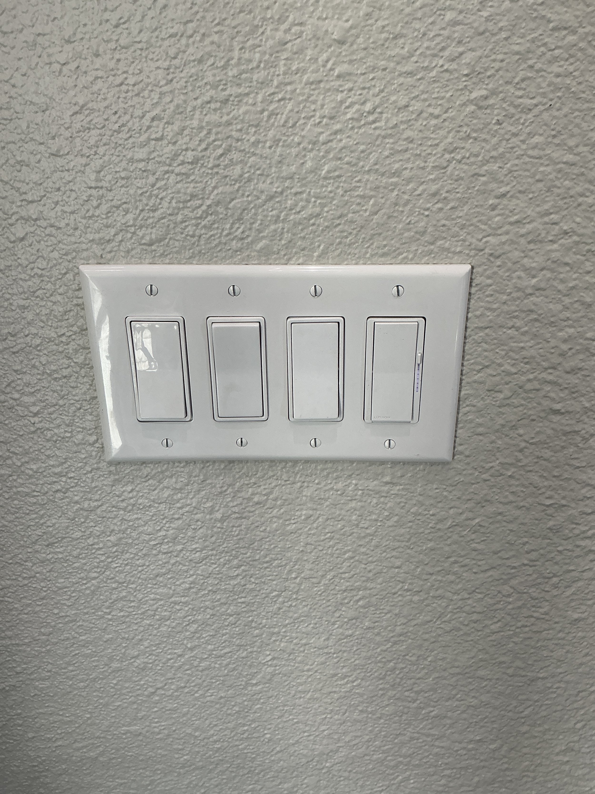 A white triple toggle light switch plate on a textured beige wall.