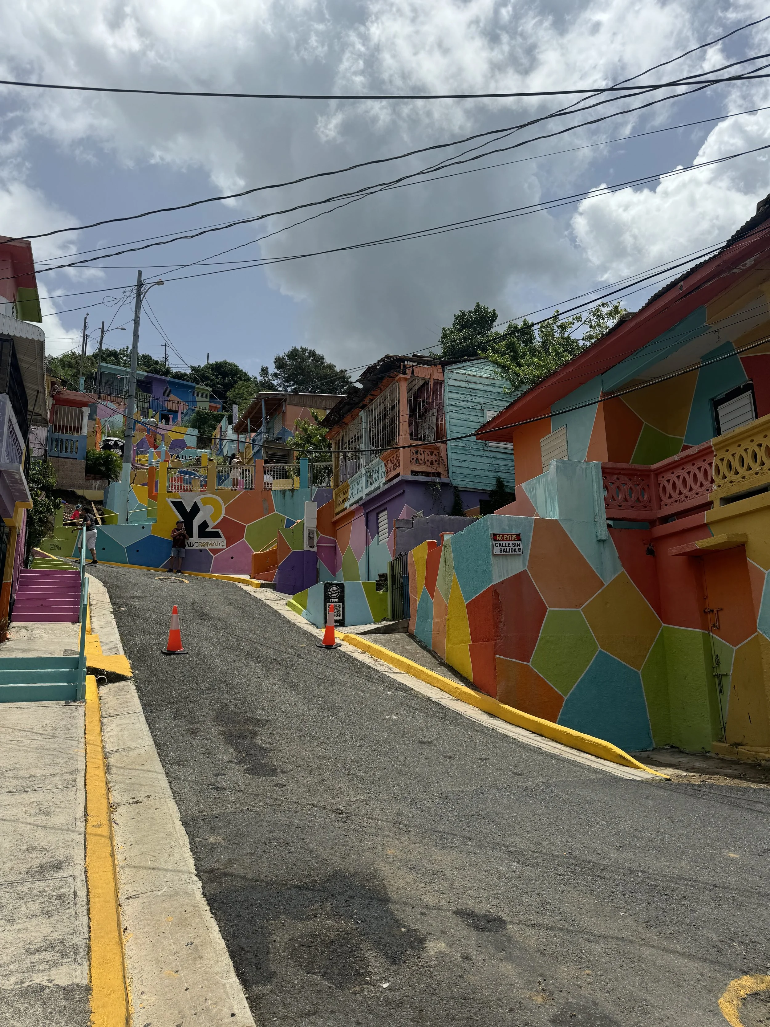 Colorful hillside neighborhood with houses painted in bright, geometric patterns, and a steep street with orange traffic cones.